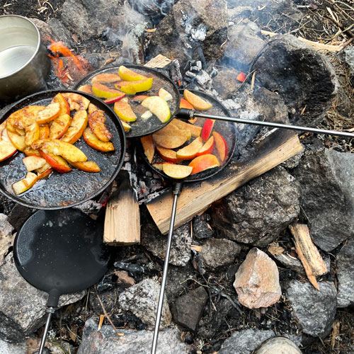 Mat som steks i stekpannor ute i skogen över en lägereld.